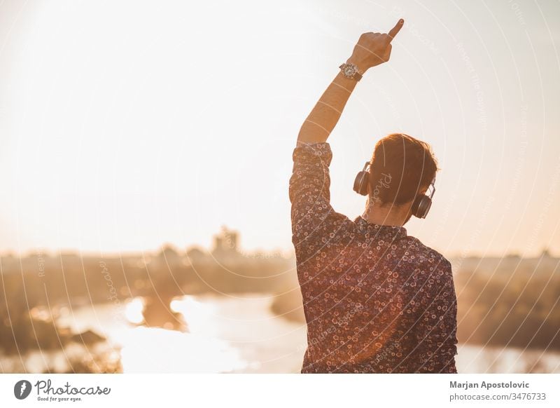 Young man listening to the music with headphones outdoors in sunset young male guy outside enjoying joyful dancing wireless technology casual lifestyle cool