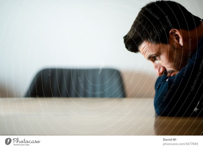 young man, lost in thought, sitting at a table Man Young man Crouch squats sits Sit Think ponder think Meditative portrait Copy Space top Table Chair