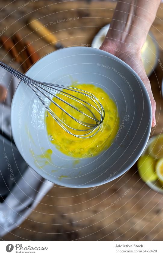 Faceless woman preparing eggs with whisk in kitchen cook ingredient bowl wooden table process food prepare cuisine fresh recipe delicious nutrition culinary