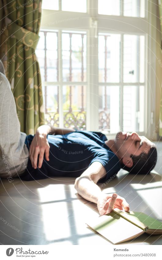 Stay at home: young man asleep on the floor while reading a book and enjoying the sunshine coming through the window. quarantine covid 19 person freedom