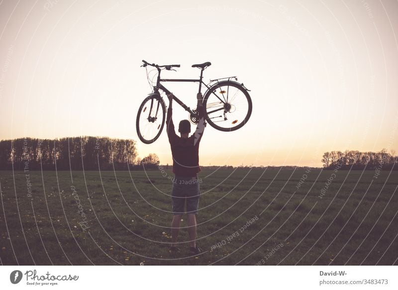 Man lifts bicycle into the air Bicycle Cycling Cycling tour Love Nature Wheel Experiencing nature out good weather Field Tall Strong strength Dusk Evening Manly