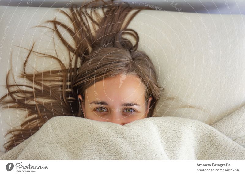 Woman in bed covered up to the face awake beautiful bedroom bedtime blanket carefree closed comfort comfortable cozy cute daydreaming eyes girl hair half face