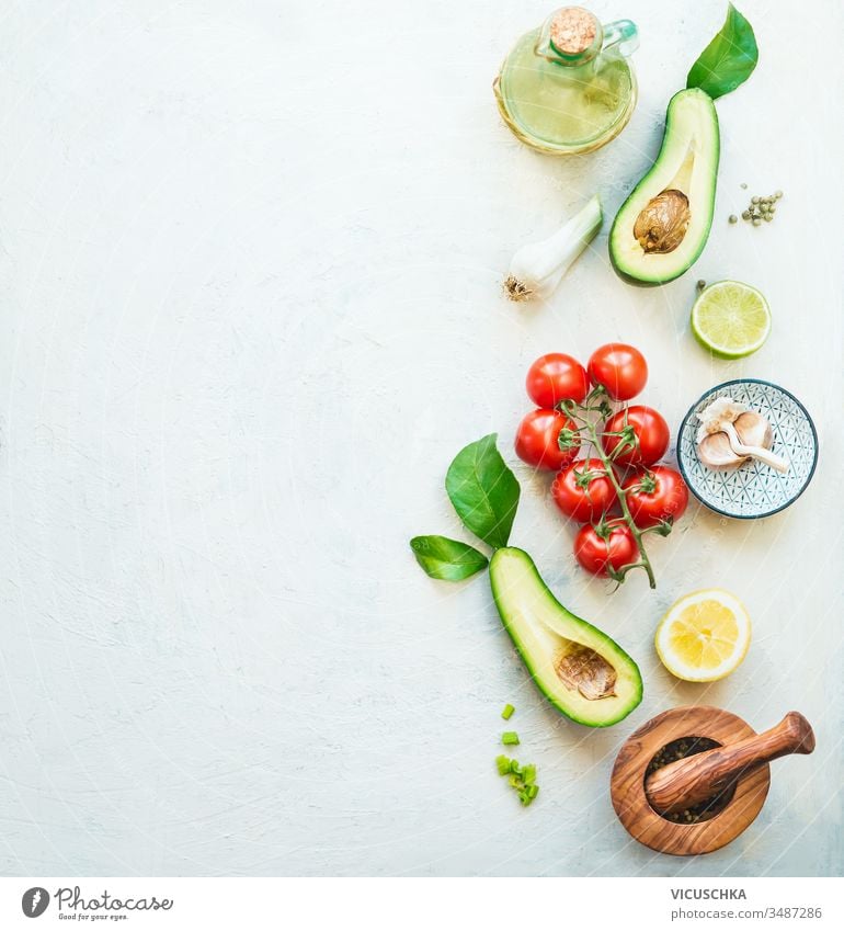 Food background with fresh salad ingredients : avocado, tomatoes, lemon , garlic and olives oil for tasty salad making, top view. Healthy food.  Vegetarian lunch or snack . Border