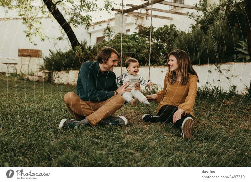 Father and mother swinging their baby sitting on the green grass in the park. Infant is laughing happy. excitement enjoyment smiling care innocent smile love