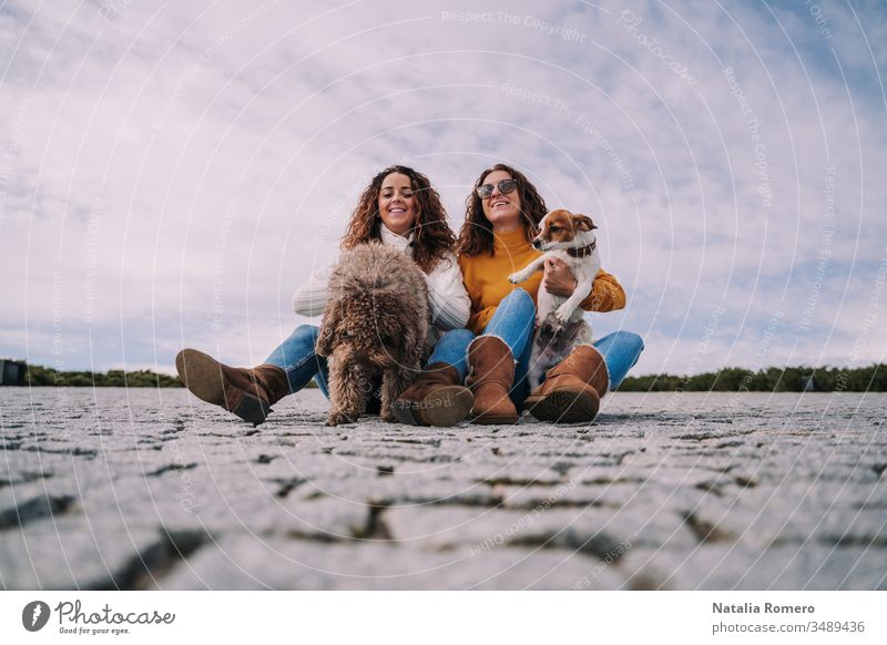 Two beautiful women are sitting in the park with their pets. They are playing and enjoying a day together. It's a cloudy day. two dog friendly people female