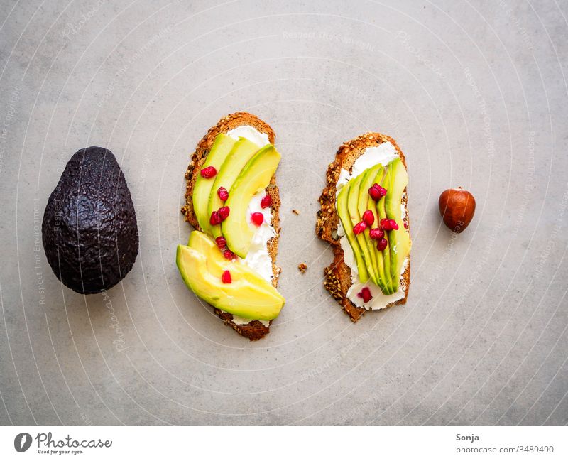 wholemeal bread with avocado and pomegranate seeds, one whole avocado and one seed on a grey background, top view, healthy breakfast Avocado Slice