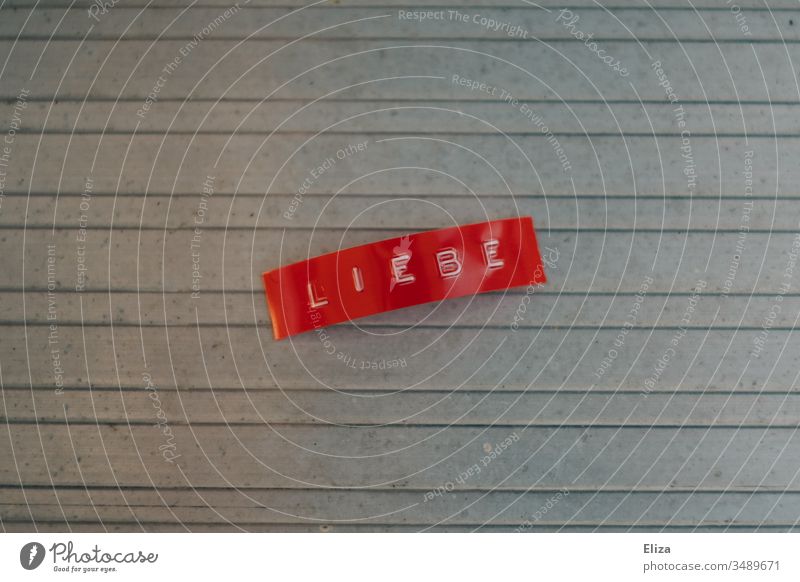 A red label with the word love written on it Love Label Word authored Letters (alphabet) Characters Deserted Gray writing Text Emotions Neutral Background Metal