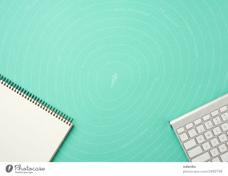 white wireless aluminum keyboard and open notebook with blank white sheets on a green background desktop tech business pc computer modern laptop office