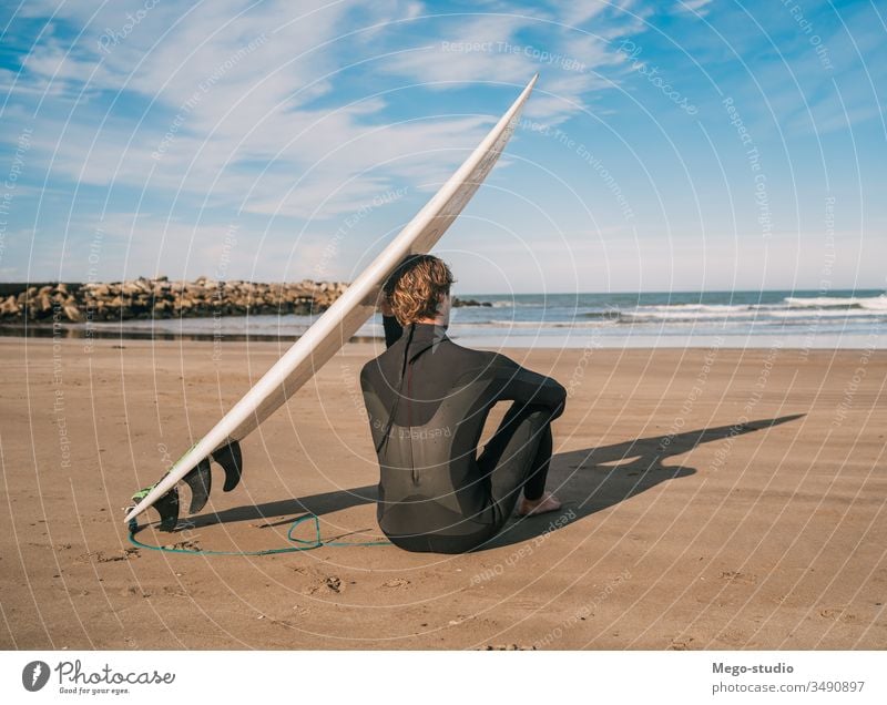 Surfer sitting on sandy beach and next to surfboard. man water sport surfing sea surfer ocean outdoors athletic coastline waves background adventure sports