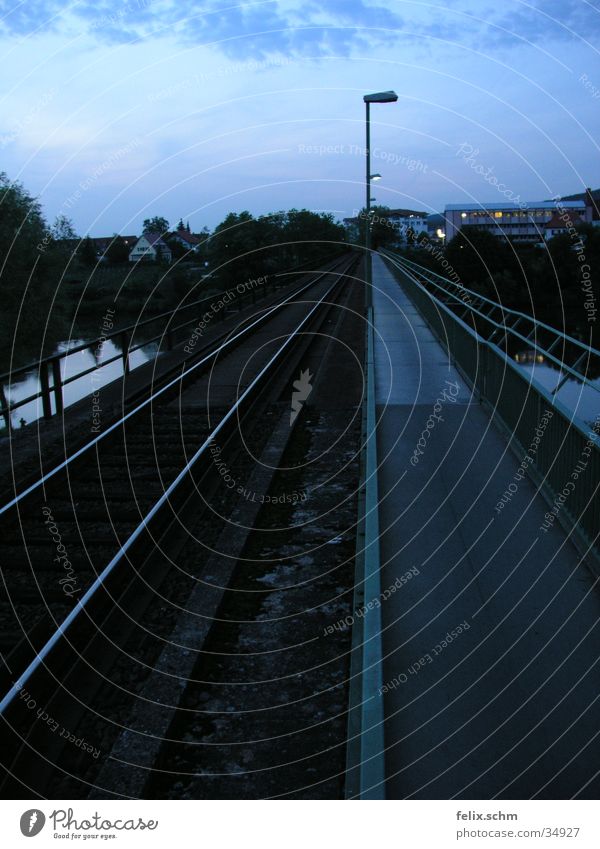 Double-track Railroad tracks Sidewalk Lantern Street lighting Junction Parallel Side by side Evening sun Twilight Horizon Bridge River branch Water Handrail