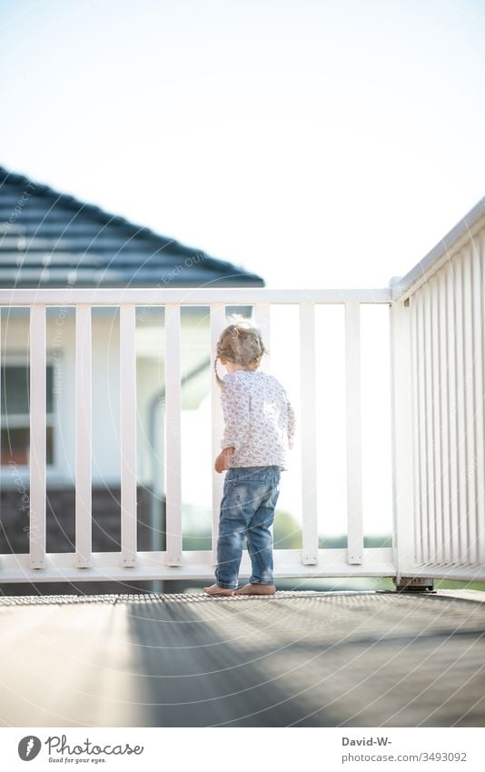 curious child girl stands on the balcony and watches from above Child Balcony Girl Cute inquisitorial Observe pretty girl Copy Space top Copy Space bottom