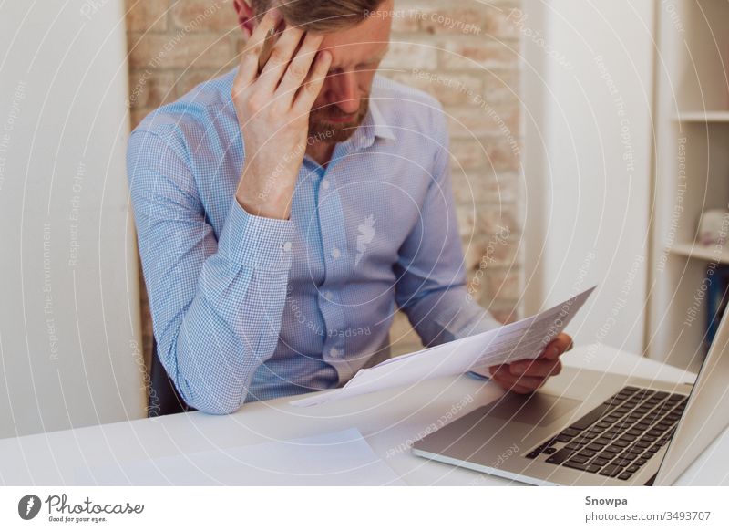 Man sitting at a desk with laptop and reading papers in light blue shirt. Light workspace, business space. Working environment. Brick wall background.