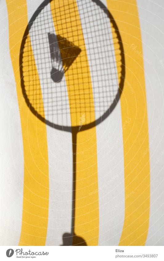 The shadow of a badminton racket with a shuttlecock in front of a striped yellow background; badminton Shuttlecock Badminton badminton rackets Badminton racket