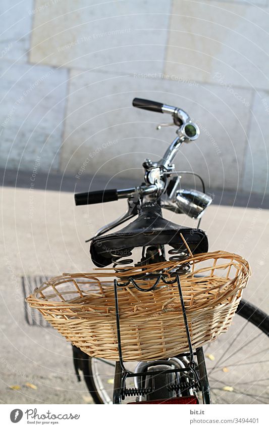 Bicycle with handlebars, saddle and basket for shopping and transport on the luggage rack is parked on the street, in the city, in front of a gray wall in the background.