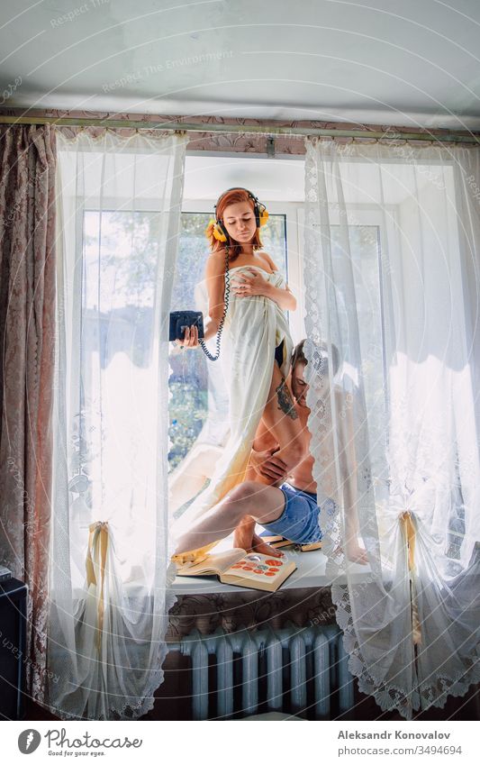 Young funny couple on a windowsill in sunshine shadows with bedsheet, vintage anatomy books, audio player and headphones laughing floor headpones mc nude