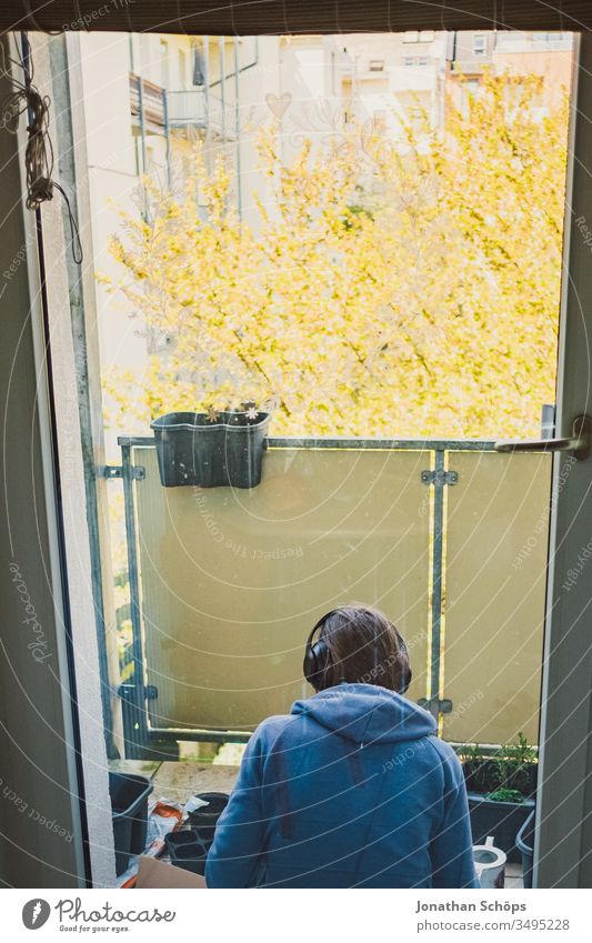 young woman sitting with headphones on the balcony facing the backyard and planting flowers and herbs outlook Balconing Balcony Balcony planting Woman hobby