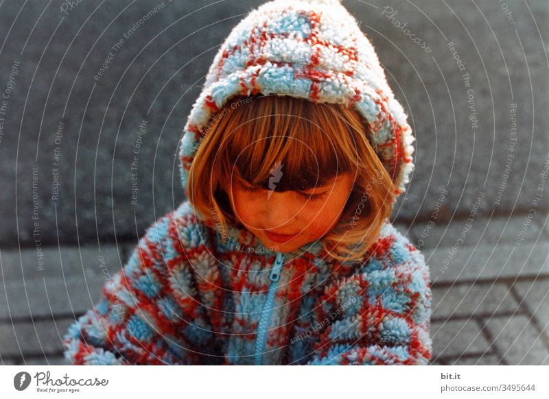 Girl in a checked fleece cuddly jacket, playing, happy, carefree and cheerful, with hood on her head, as weather protection, out on the street in autumn.