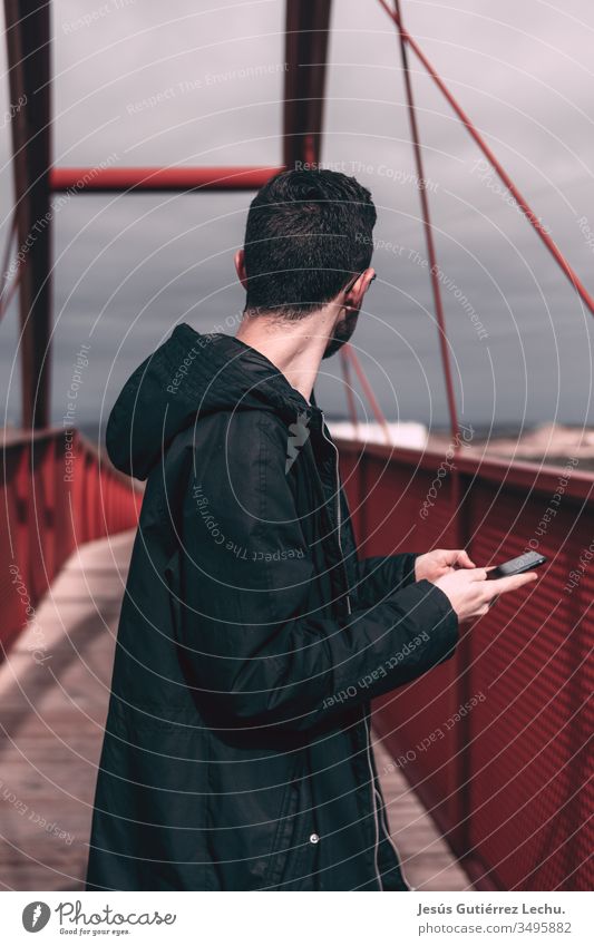 man in a black coat holding a mobile phone on a red bridge Day Town Bridge building Vacation & Travel Architecture Bridge pier Sky City trip Colour photo