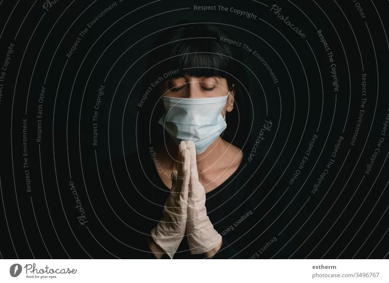 young woman wearing medical mask for coronavirus with hands clasped together praying covid-19 2019-ncov epidemic pandemic quarantine stay home playing prayer