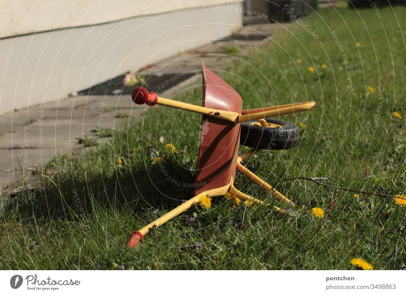 Children's toy wheelbarrow stands upright on a meadow. Gardening Wheelbarrow Toys Meadow Dandelion Green Nature hobby Playing Gardener Grass Colour photo