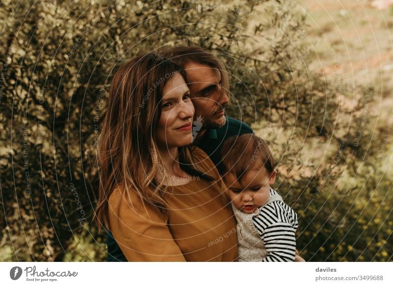 Couple standing with their son outdoors. Young family concept. Mother holds the baby in the arms. Man and woman look away relaxed. happy park people young