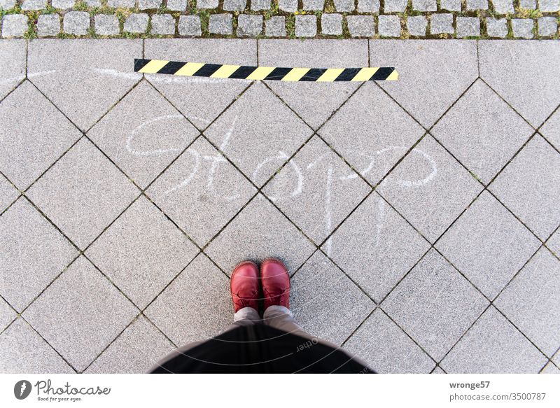 Yellow and black barrier tape and the word stop on the sidewalk invite a female person to keep her distance in times of Corona yellow-black Hold gap Stop line