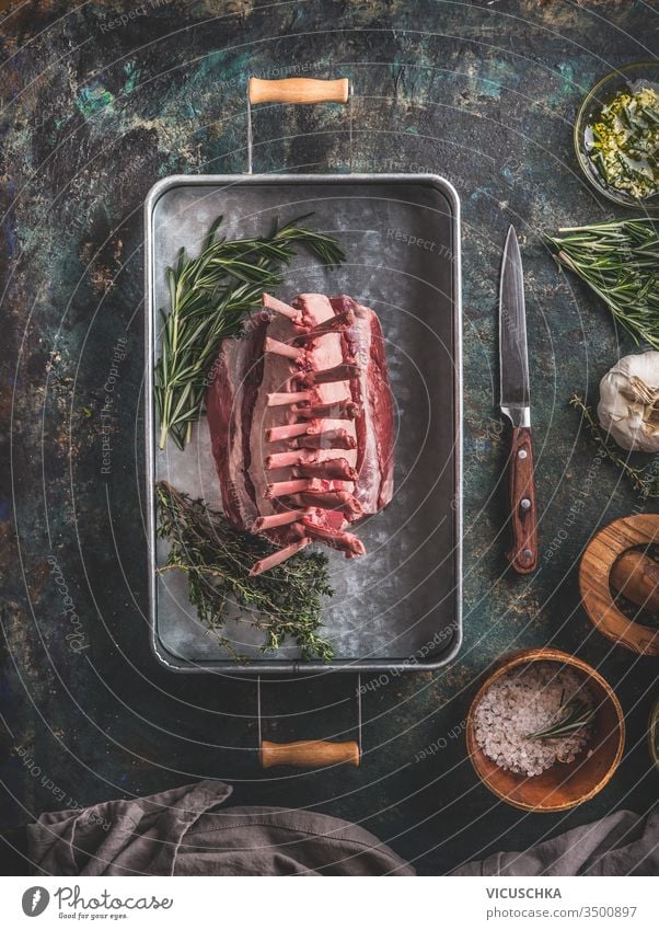 Raw lamb racks preparation on dark rustic kitchen table background with herbs und spices. Top view. Meat food. Lamb crown roast making raw top view meat