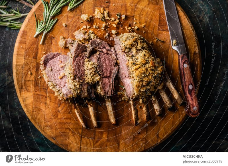 Close up of crusted lamb ribs cutlets with bone rar medium roasted on wooden cutting board with knife and herbs. Top view. Meat food close up top view meat