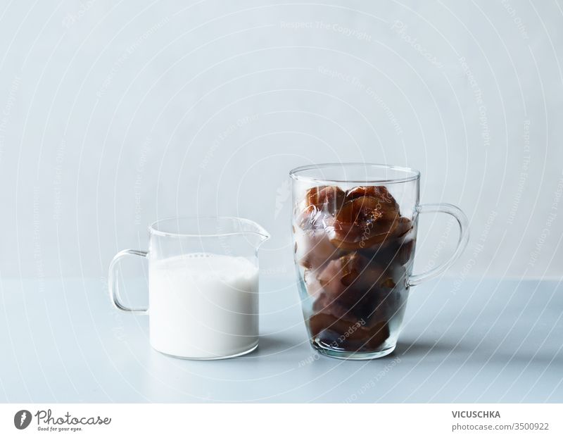 Coffee ice cubes in glass mug and little jug with cream or vegan milk on grey table at wall background. Refreshing summer drinks making ingredients coffee