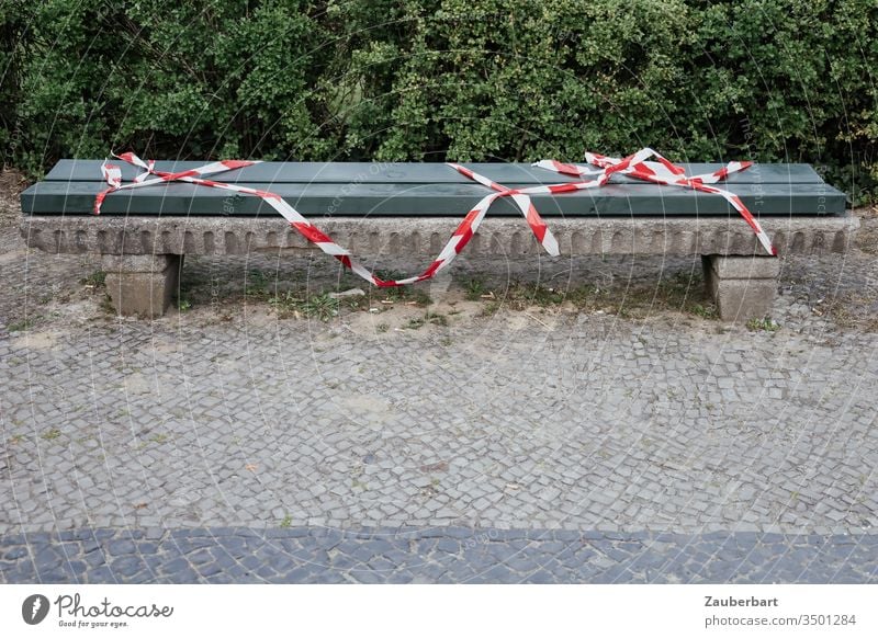 Bank with red and white barrier tape because of Corona Bench cordon Band Red White covid-19 coronavirus pavement Paving stone Wood Green Boxwoods containment