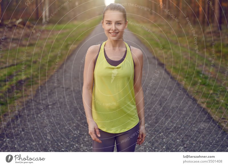 Smiling athletic fit young woman working out on a tarred lane through forests backlit by the warm glow of the sun in a healthy active lifestyle concept face