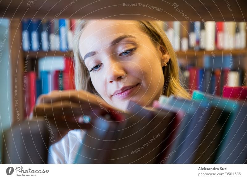 Young girl standing in traditional old library at bookshelves, looking for books. Close-up smiling student searching, studying. Higher education. academic