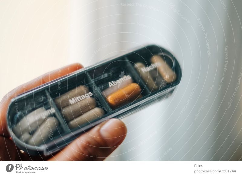 A person holds a medicine box in which different tablets and pills are sorted for the different times of day drugs Nutrional supplement diverse Tin pill box