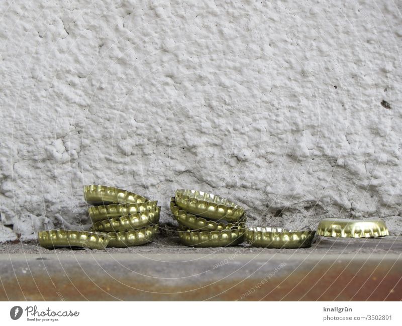 Ten crown caps, partly stacked, are lying in front of a plastered house wall Crown cork Bottle lid Metal Lie waste Alcoholic drinks Beer alcohol consumption