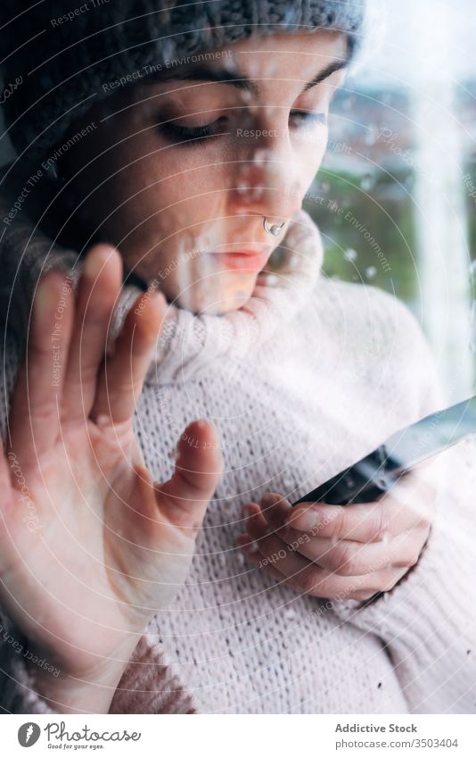 Young woman with smartphone standing near window home using lonely sad self isolation browsing gadget coronavirus covid-19 quarantine young female casual