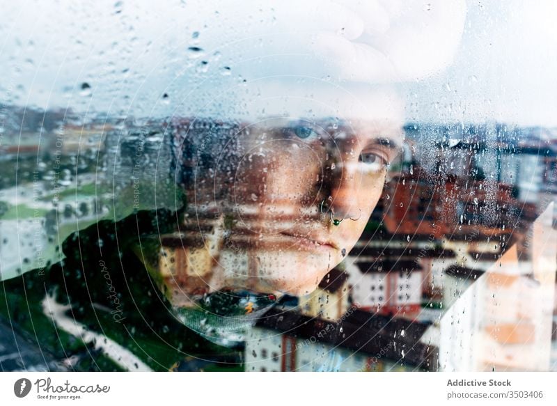 Depressed man looking through window sad depression isolation coronavirus home desperate lonely unhappy young male wet rain melancholy solitude stress frustrate