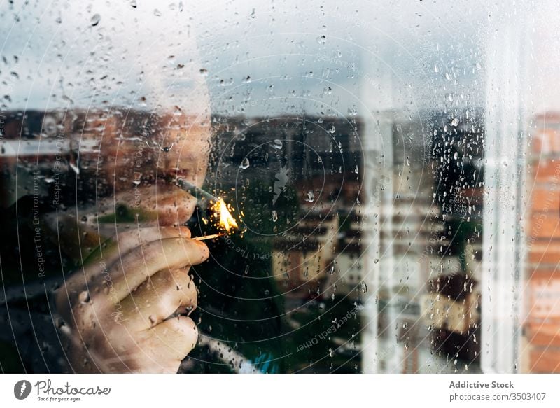 Man smoking cigarette near window at home man smoke lonely sad wet depression coronavirus tranquil self isolation desperate unhappy young male rain melancholy