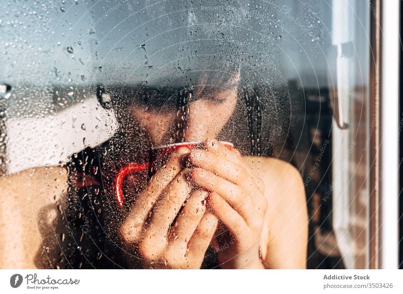 Thoughtful woman drinking coffee near window sad depression self isolation home unhappy lonely covid19 melancholy young female wet rain solitude stress cup