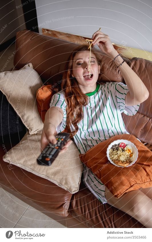 Young female eating noodles and watching TV woman ramen tv home lunch young rest japanese sofa film movie change channel remote control tradition authentic