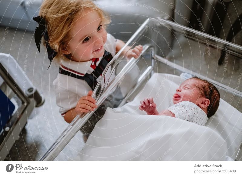 Happy girl standing near newborn sibling baby sister happy sleep hospital crib cradle child kid little care childhood neonatal together childcare cheerful love