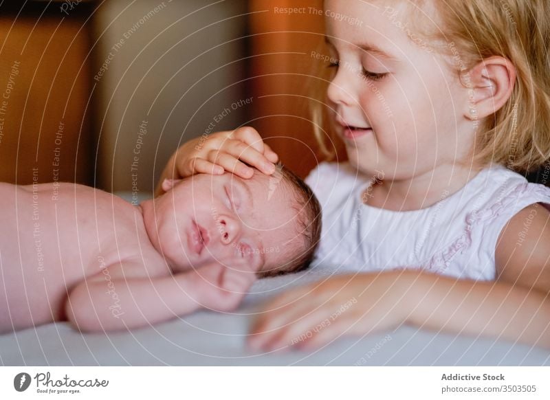 Happy small girl caressing with love newborn sleeping in soft bed at home kid sister infant calm relax innocent sibling rest little child interest friendly face