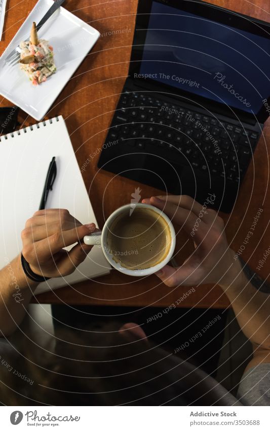 Freelancer sitting at cafe table and drinking coffee man sketch notebook freelance laptop remote project male draw notepad cup student cafeteria computer