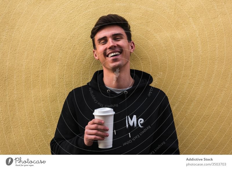 Cheerful man with drink to go resting on street modern beverage takeaway social media city relax exterior horizontal coffee cheerful tea guy lean lifestyle town