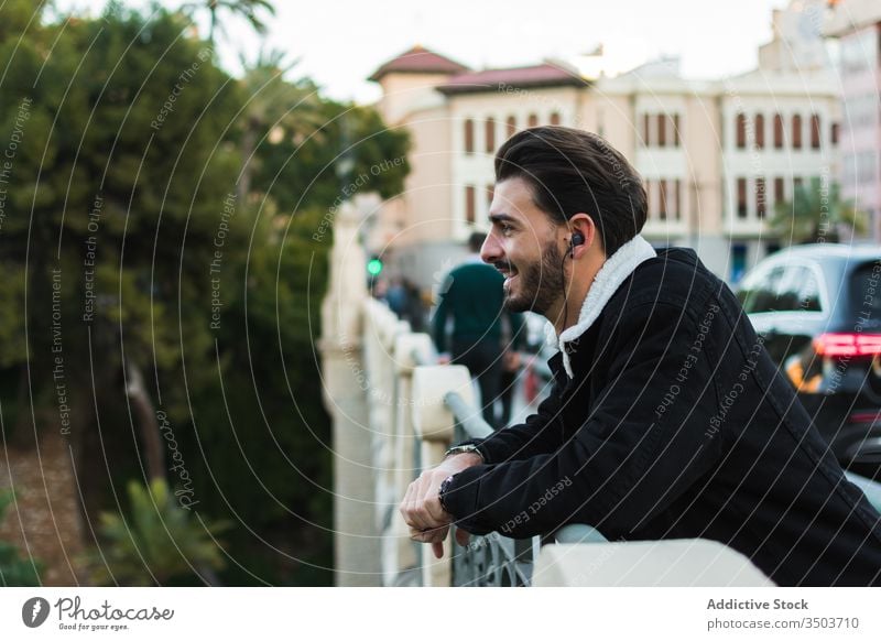 Happy man with earphones standing on city bridge happy listen street rest relax enjoy music lifestyle male ethnic trendy smile young cheerful device season