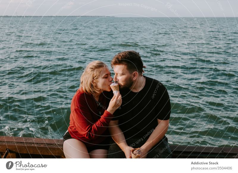 Loving couple eating ice cream together sea romantic enjoy love relationship rest holiday happy young casual summer vacation date married travel sit relax