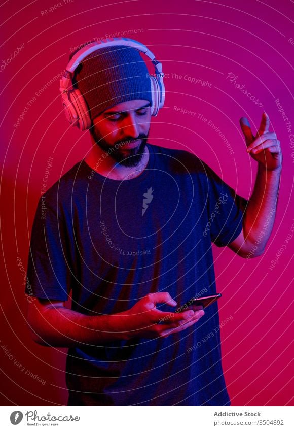 Modern man using smartphone and listening to music shaka sign modern style mobile phone red light male device gadget gesture headphones young beard sound