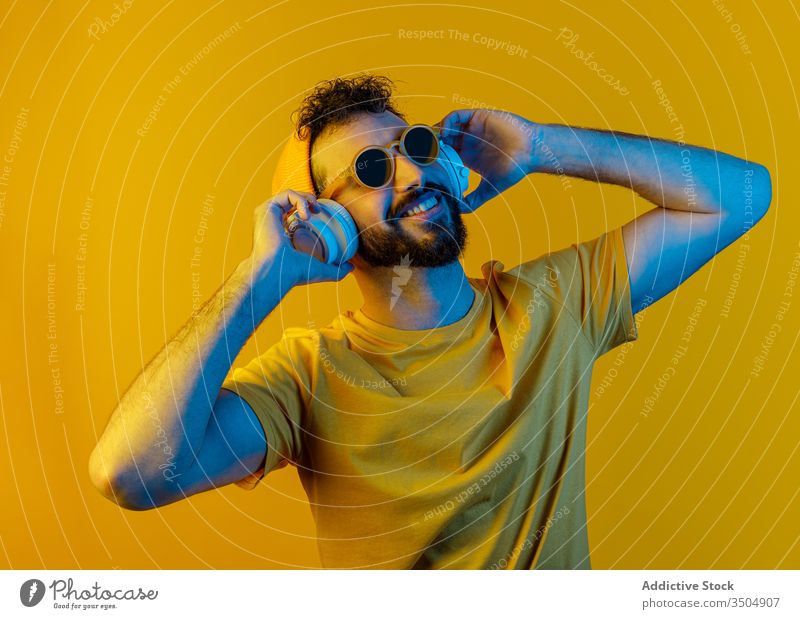 Bearded man with modern headphones urban style outfit music color bright male contemporary white yellow accessory hat sunglasses sound melody tune vivid vibrant