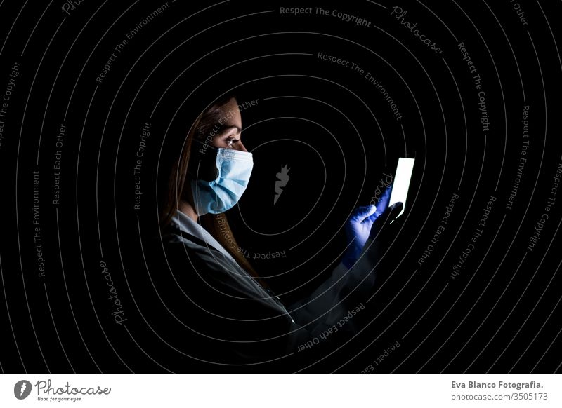 doctor woman indoors, using mobile phone. Wearing protective gloves, mask and stethoscope. coronavirus covid-19 concept internet tecgnology dark corna virus