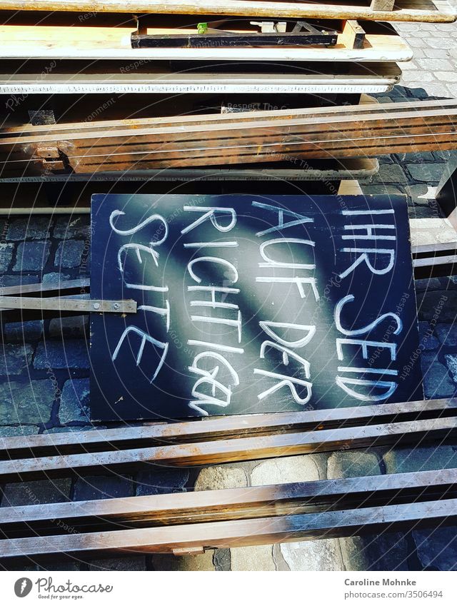 Black board with white writing "YOU ARE ON THE CORRECT SIDE" lying on the floor between the fixed benches and the construction material lettering Characters