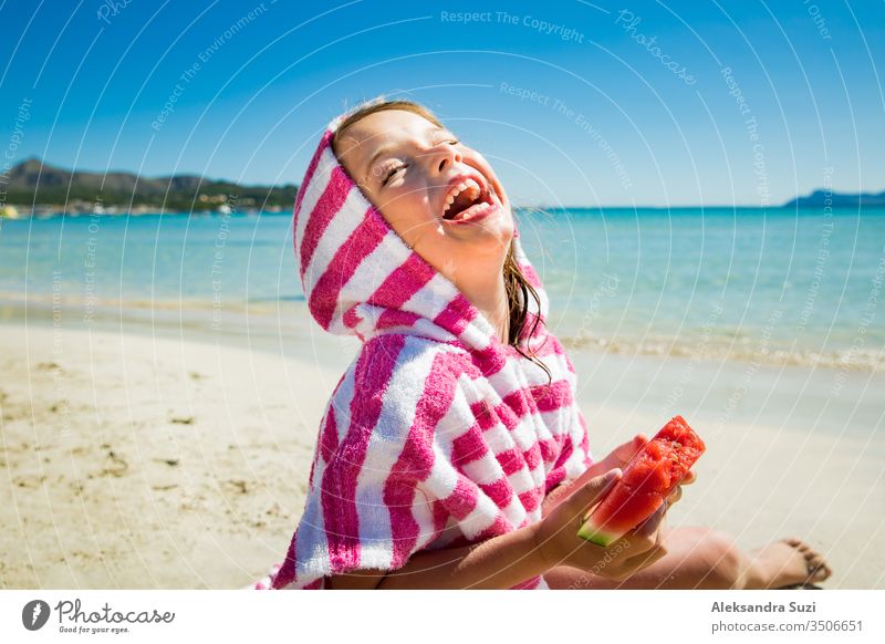 Cute happy little girl eating watermelon and laughing on the sand beach. Turquoise sea, blue sky, sunny summer day. Majorca, Spain activity beautiful candid